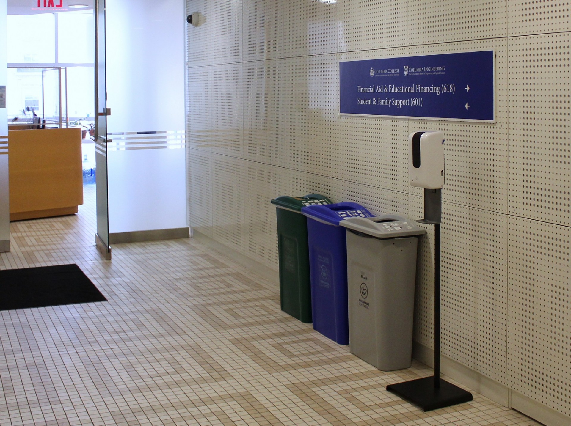 Recycling bins and a waste bin sit in a central hallway outside an office in Lerner Hall